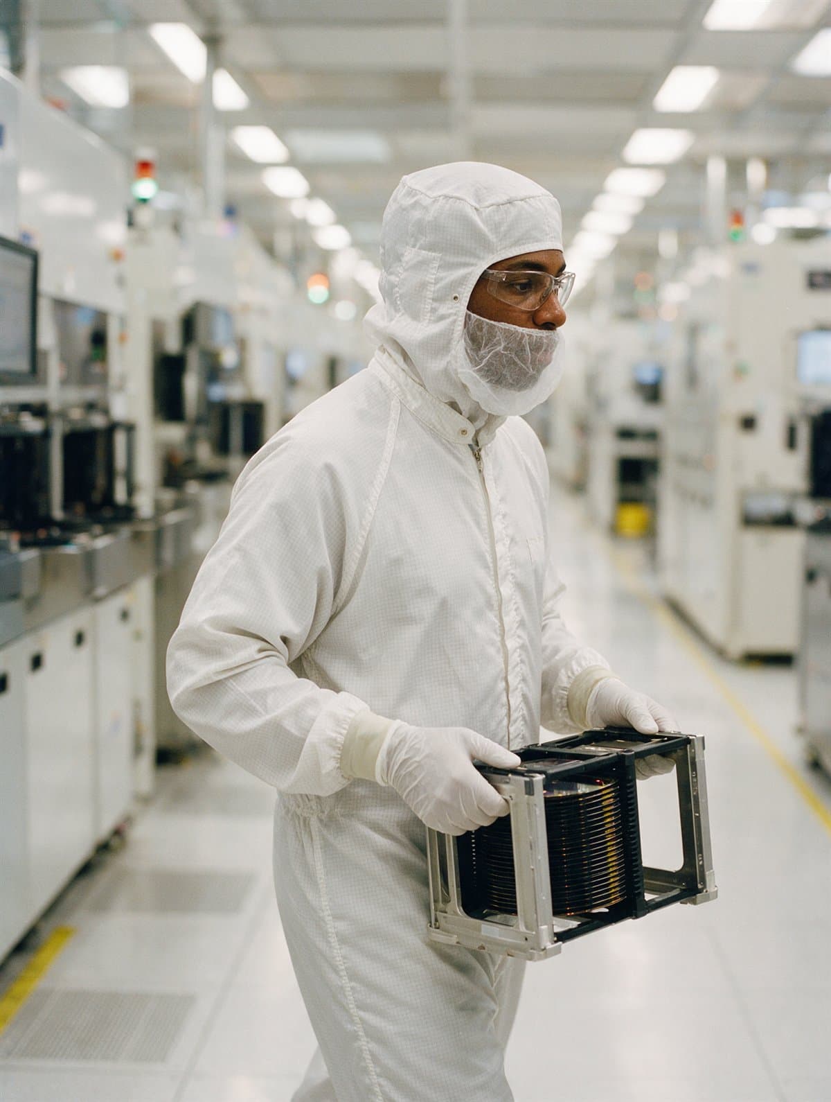 A cleanroom operator carrying a wafer carrier along a tool aisle
