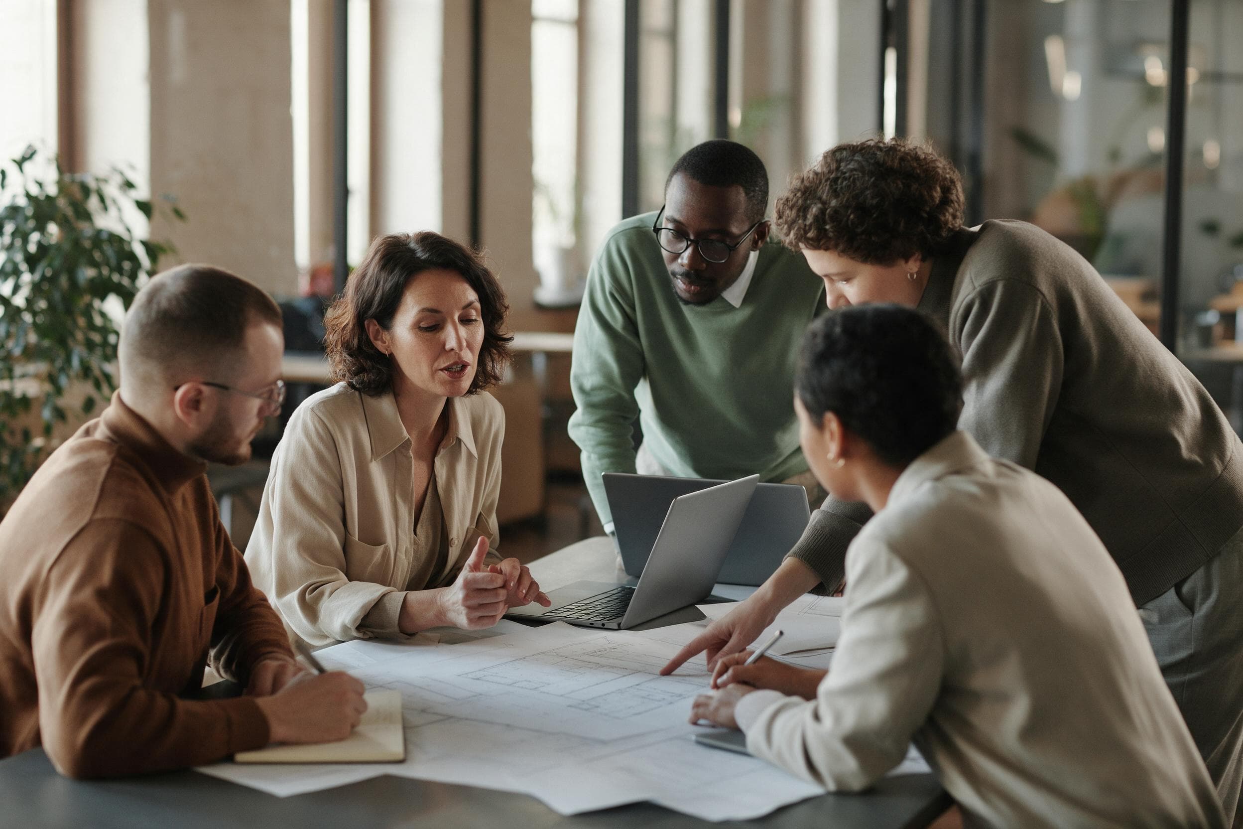 A cross functional team of five around a table in a modern office, working through printed plans together